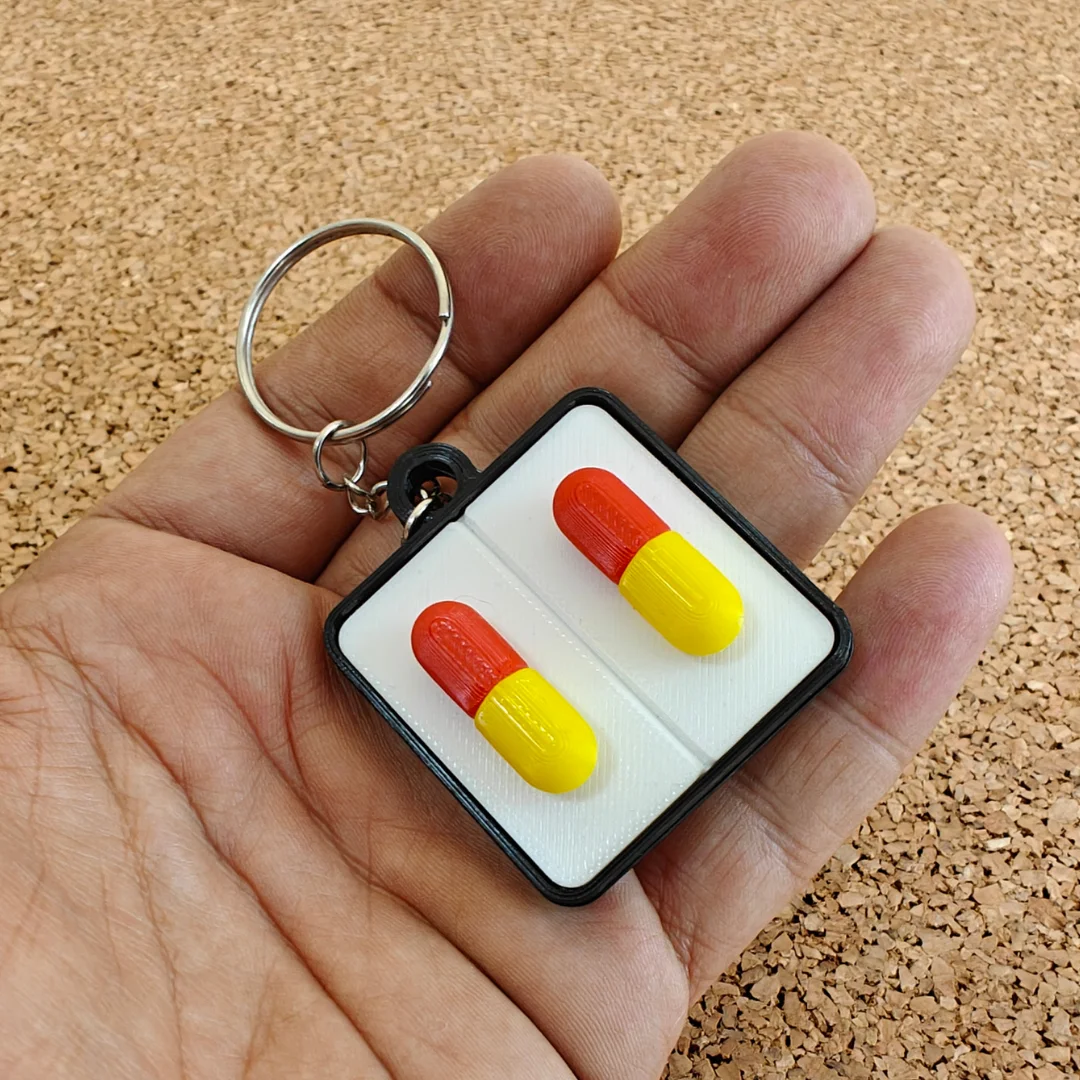 Capsule keychain held in a hand, showing two raised capsule shapes.