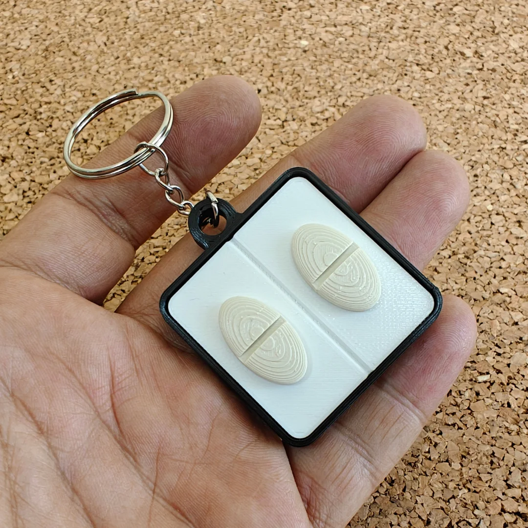 Oval pill keychain held in a hand, showing raised pill details and compact size.