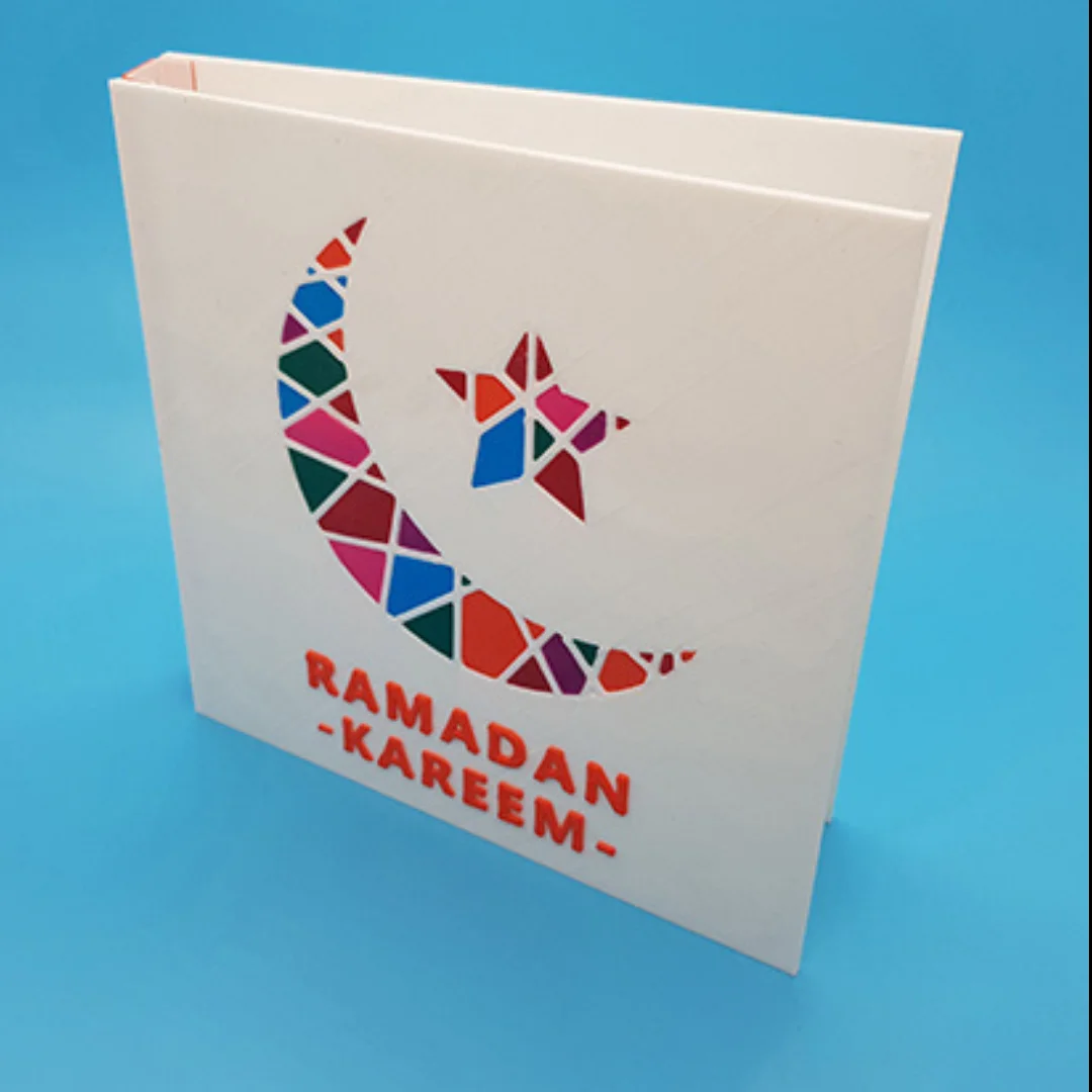 Angled view of a Ramadan Kareem card with a geometric crescent and star design.