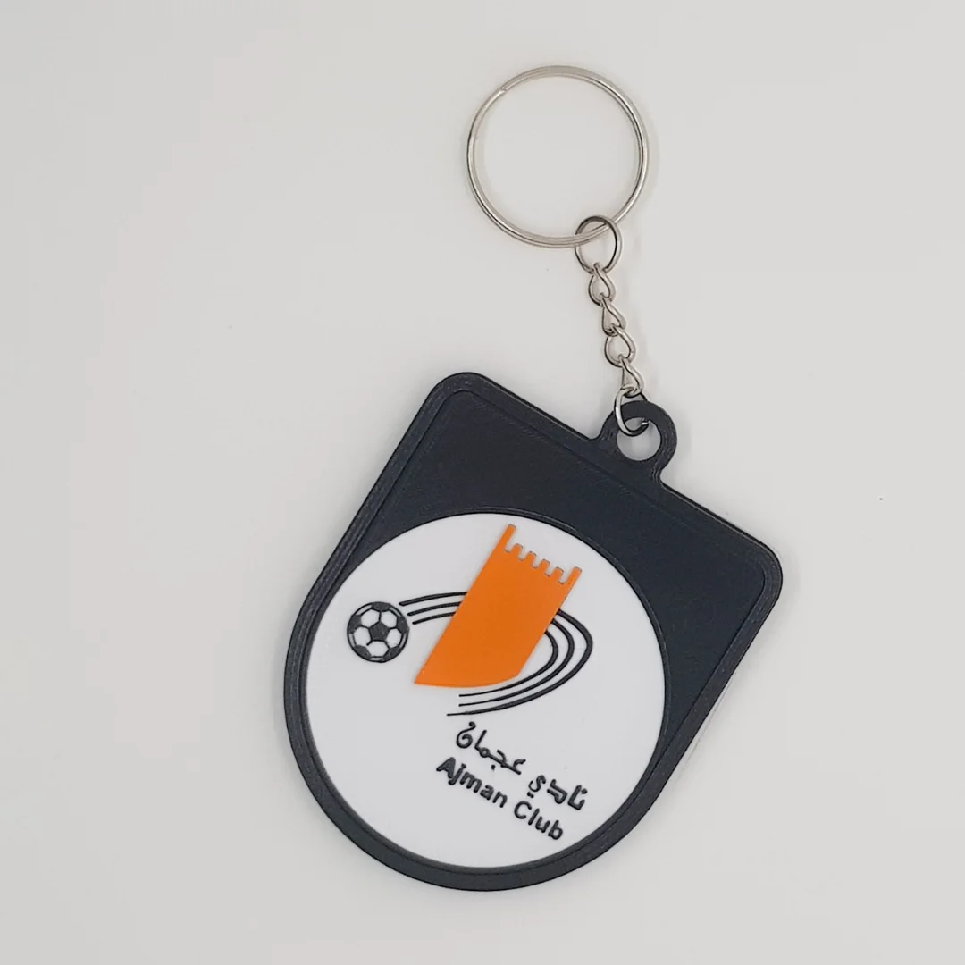 Front view of the Ajman Club crest keychain with its chain and metal ring.